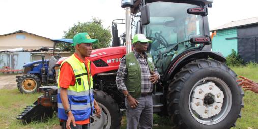 Dr. Arthur Bob Karnuah, Director General of CARI, and Daniel Wiagbe, National Coordination Officer of the SADFONS Project, pose together during the official handover of advanced 90‑horsepower tractor accompanied by multiple implements, power tillers, and motorized sprayers.